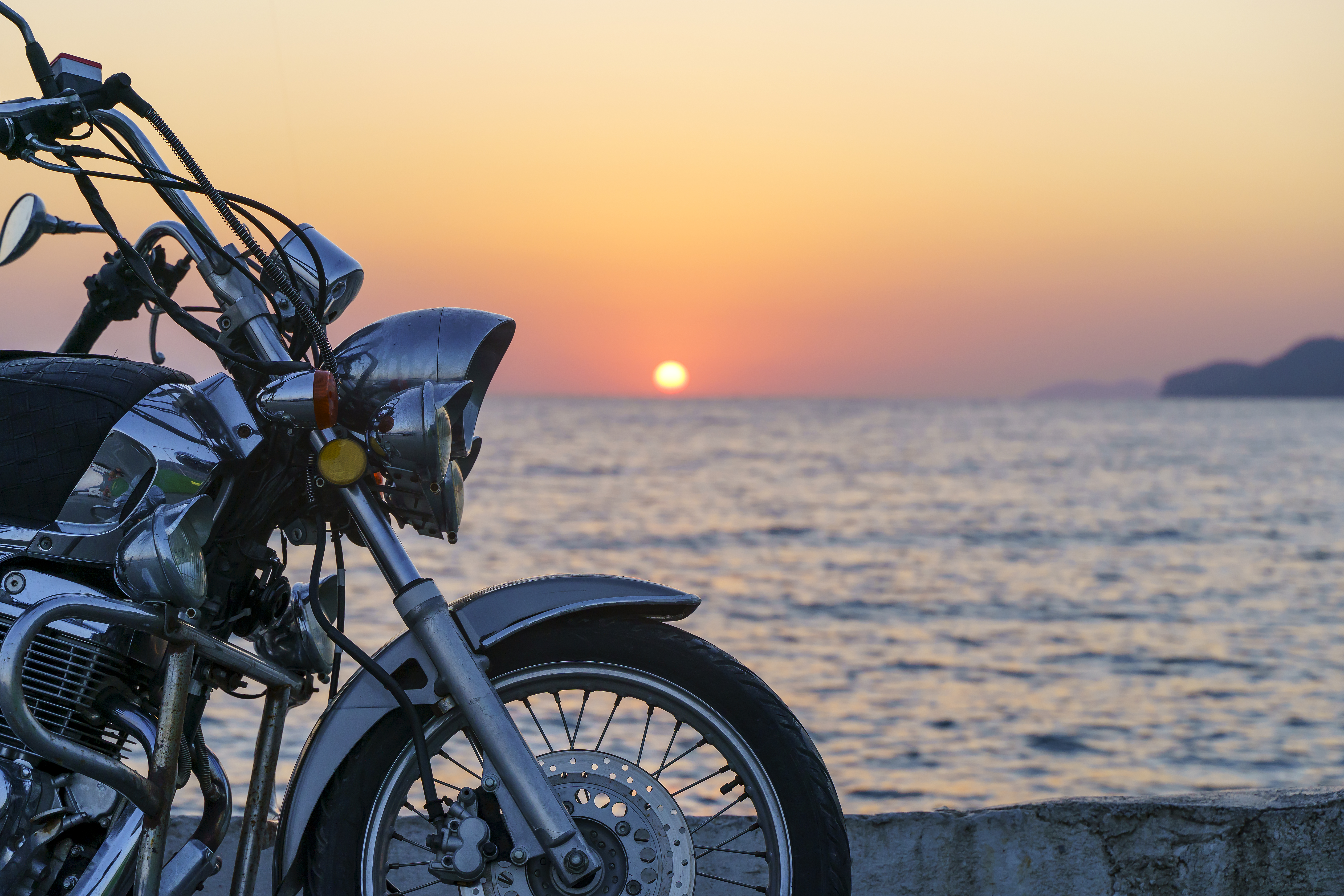 Front half of motorcycle parked in front of a body of water at dusk.