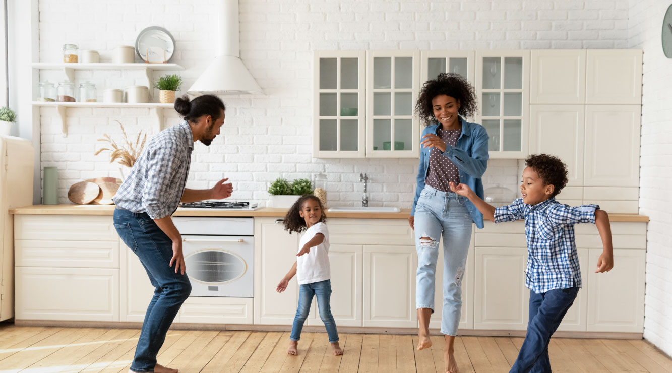 Family of two parents and two children dancing in a kitchen setting.