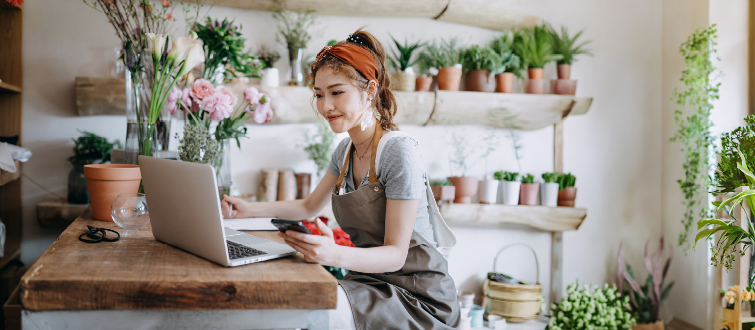 Image of a woman sitting at a laptop in a floral shop setting.