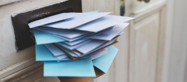 Image of an mail slot in a door stuffed with envelopes of varying colors and sizes.