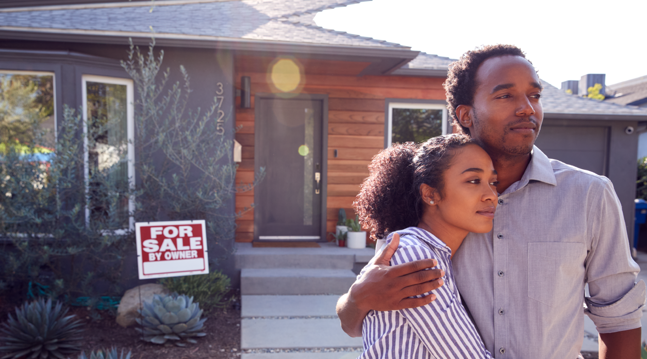 Couple standing in front of house with a For Sale sign