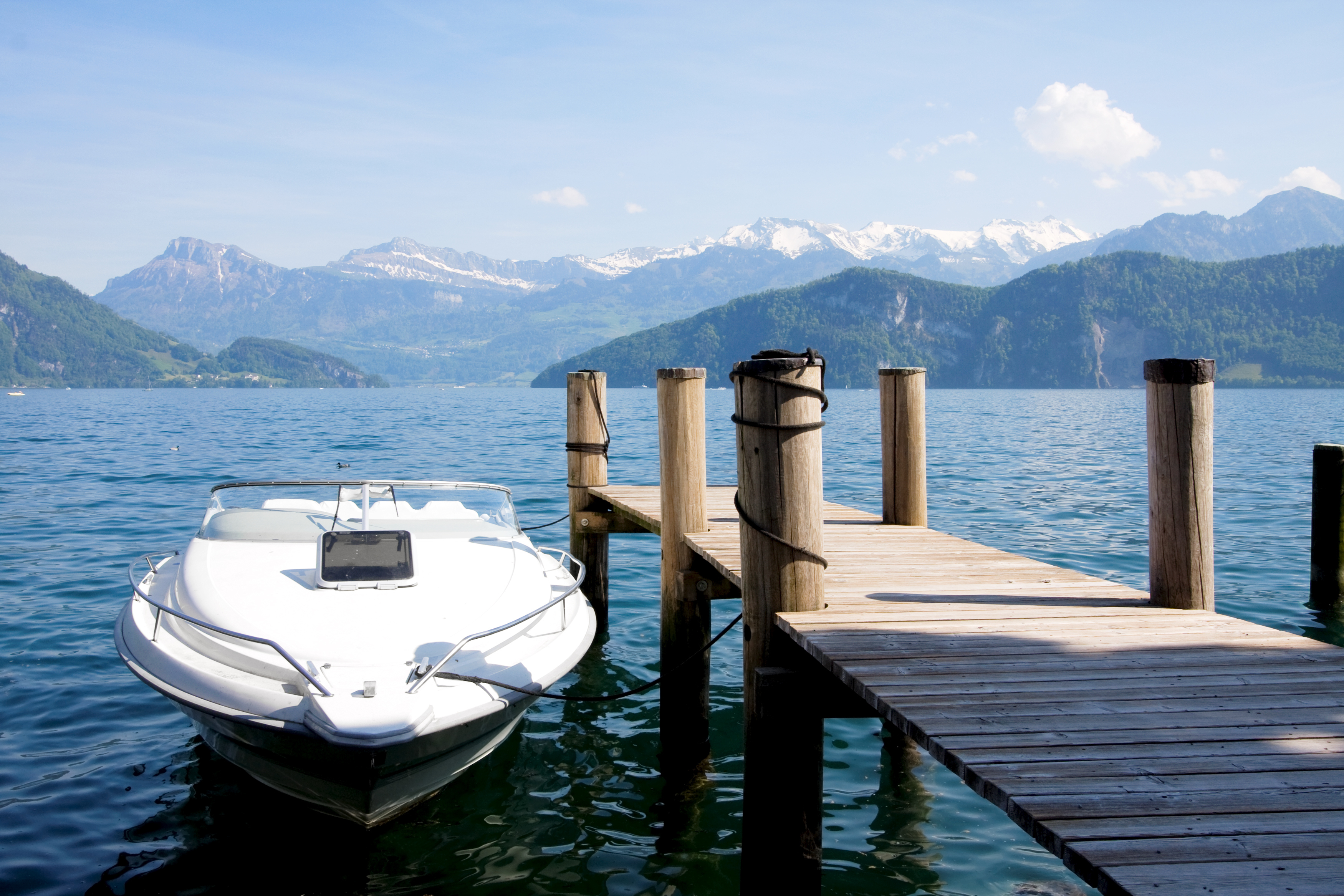 White boat tied to a wood doc on a lake with snow-capped mountains in the background.