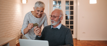 Man and woman holding a credit card in front of a laptop, smiling