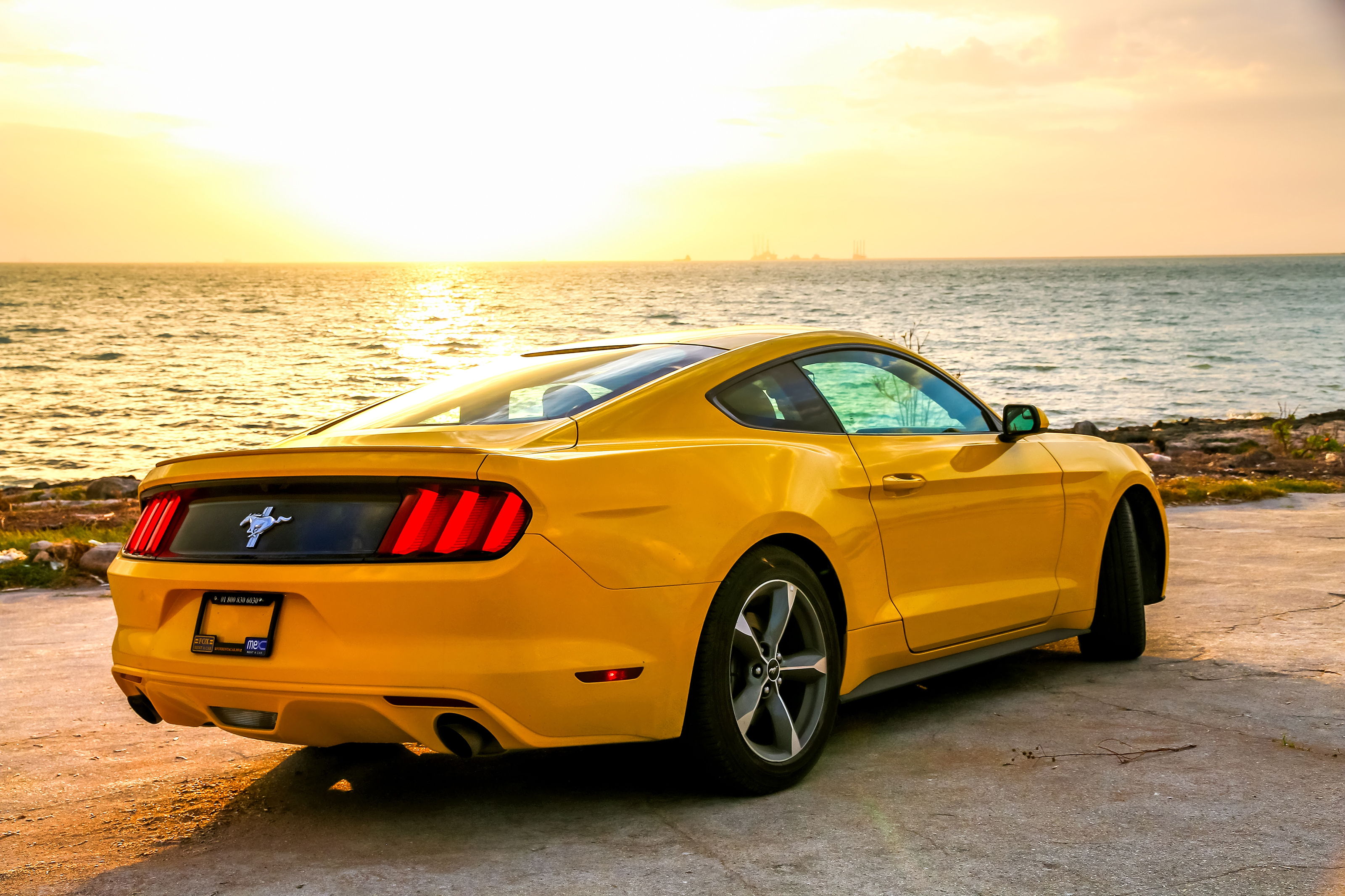 Yellow sports card parked on a coastline with a sunset over a body of water